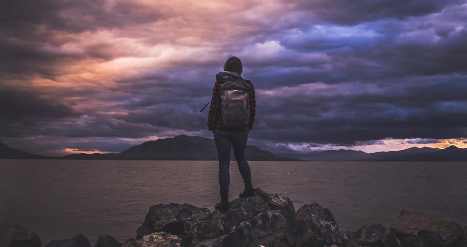 Foto eines Backpackers zur blauen Stunde, der in einen Himmel schaut