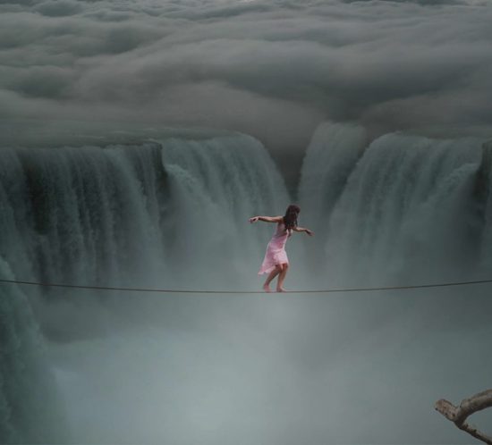 Foto einer Frau in rosanem Kleid, die auf einem Seil einen Wasserfall überquert