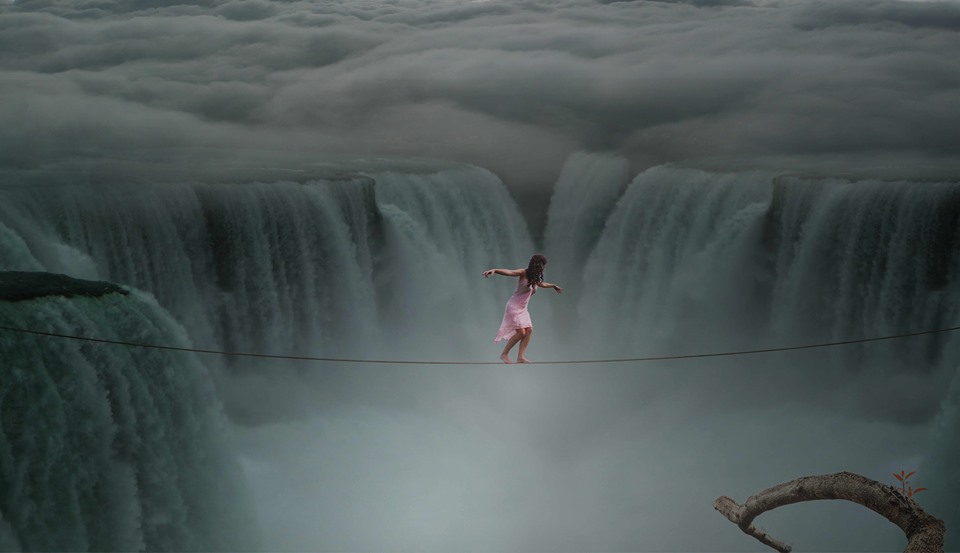 Foto einer Frau in rosanem Kleid, die auf einem Seil einen Wasserfall überquert